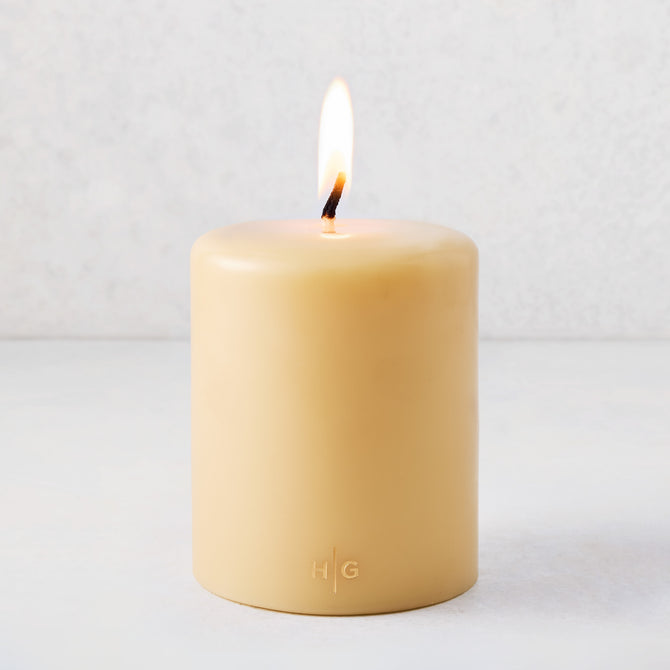 5" x 6" amber unscented pillar candle with a lit cotton wick and gold HG logo embossed on the front.