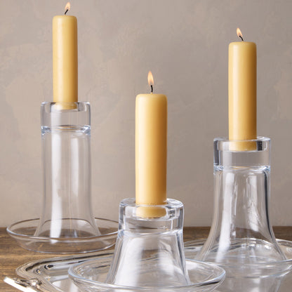 Three lit HG Amber Unscented Taper Candles, 7" x 1 3/4", in clear glass Luz Candleholders on a silver tray.