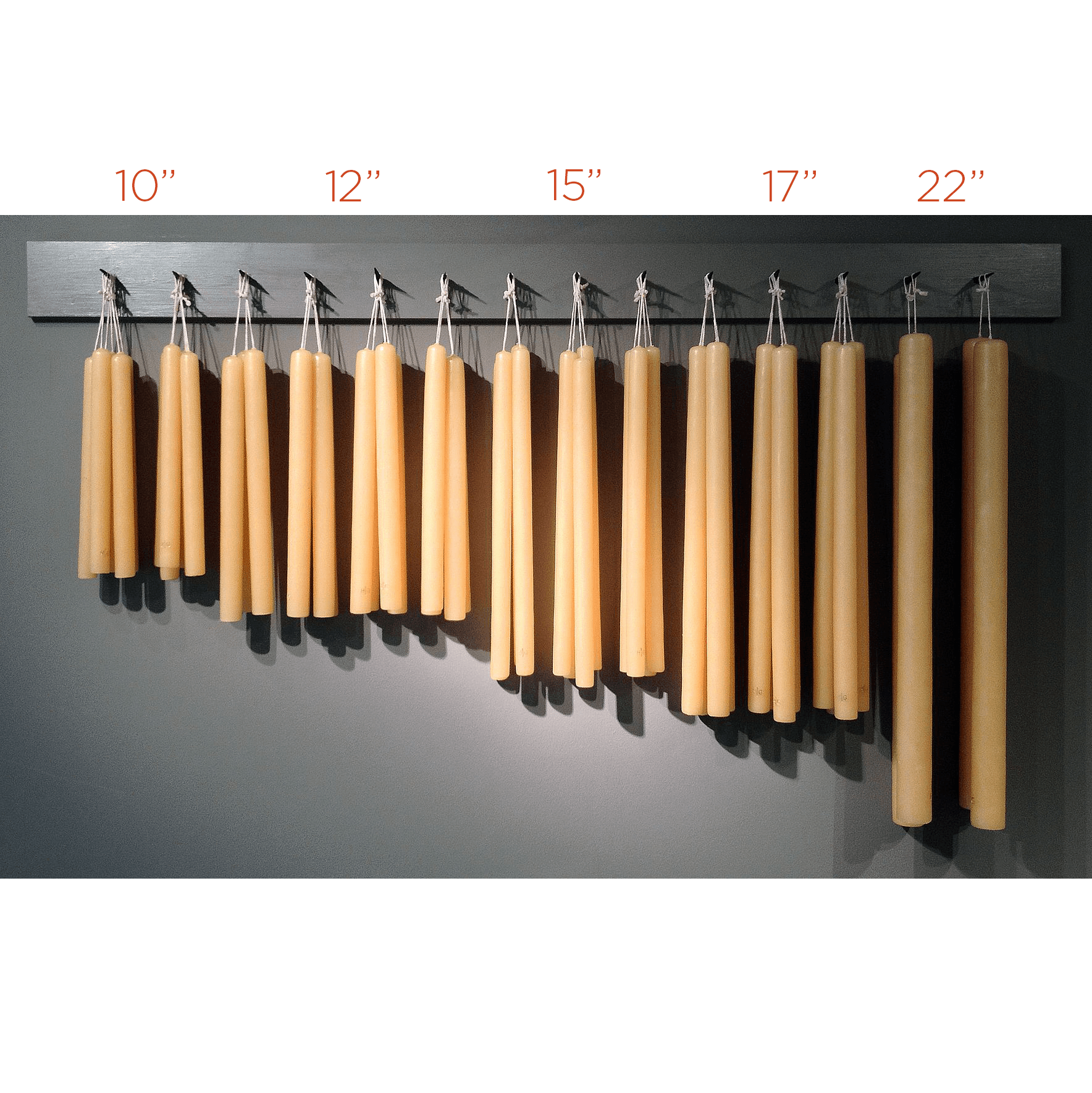 Five sets of HG Amber Unscented Taper Candles in various sizes, from 10" to 22", hanging on a dark rack.