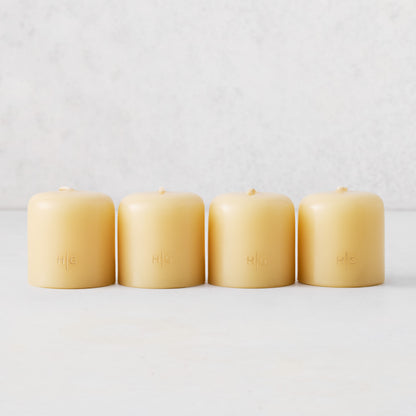 Set of four 2-inch amber unscented votive candles with gold embossed HG logo on a white surface.