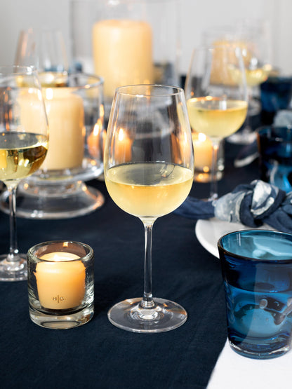HG Amber Unscented 2" Votive Candle in a glass holder, with a gold HG logo, on a dark blue tablecloth.