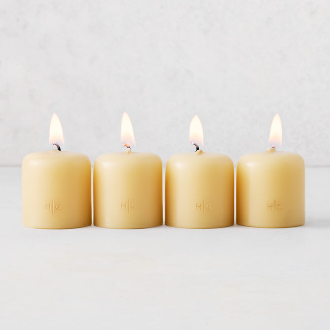 Set of four 2-inch amber unscented votive candles with lit wicks and embossed gold HG logo on a white background.
