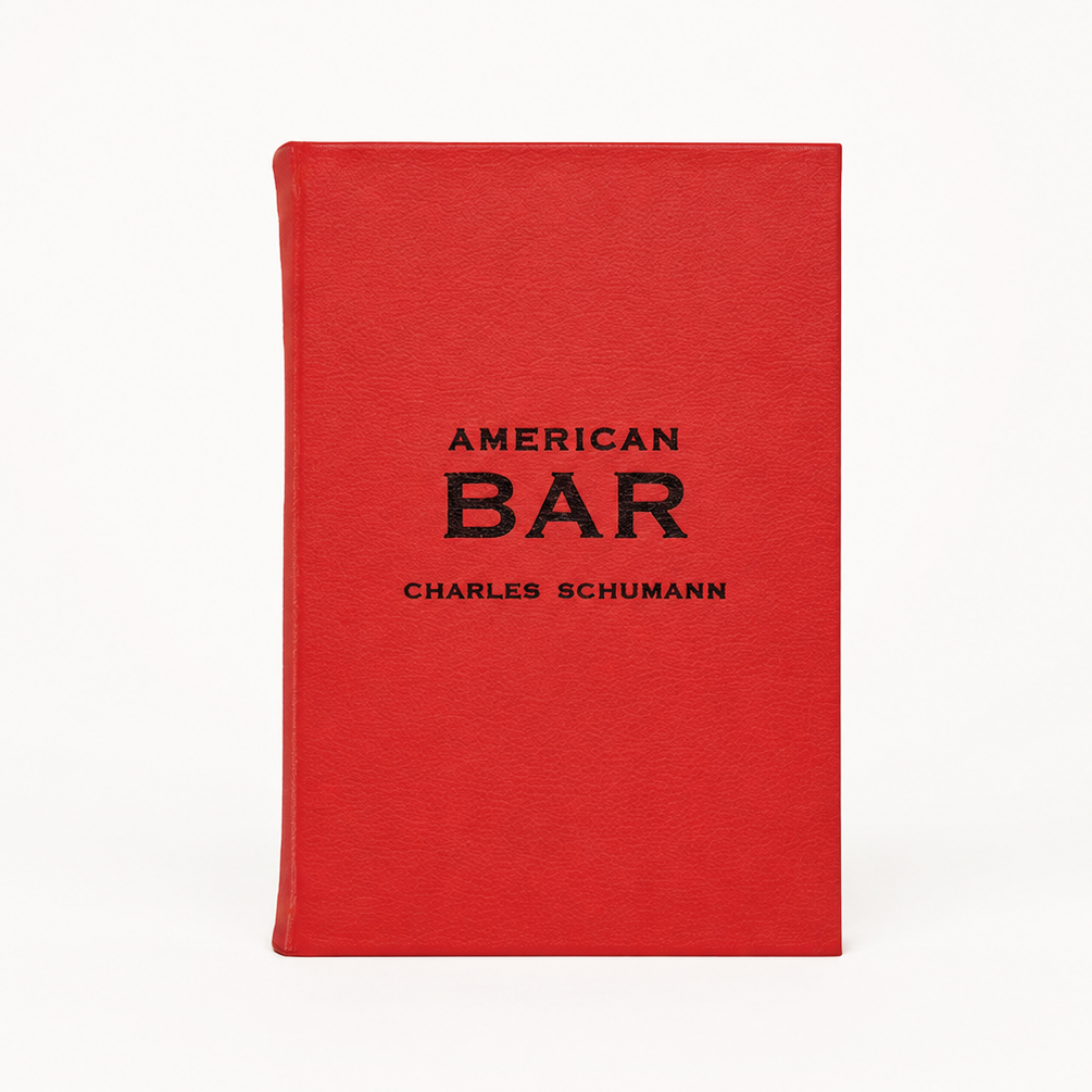 American Bar by Charles Schumann, a red leather-bound cocktail recipe book with black embossed text on the cover.