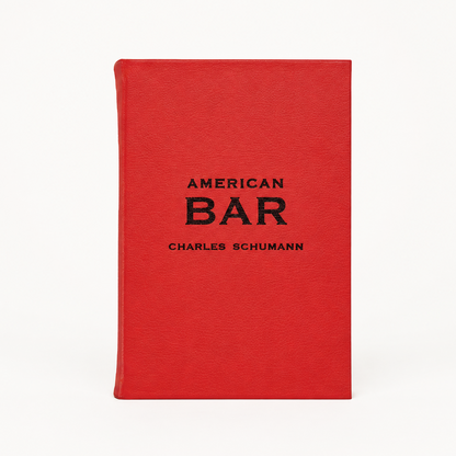 American Bar by Charles Schumann, a red leather-bound cocktail recipe book with black embossed text on the cover.