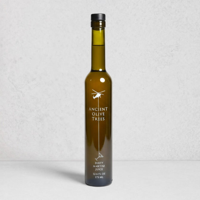 Ancient Olive Trees Dirty Martini Juice in a tall, dark green glass bottle with a black cap.