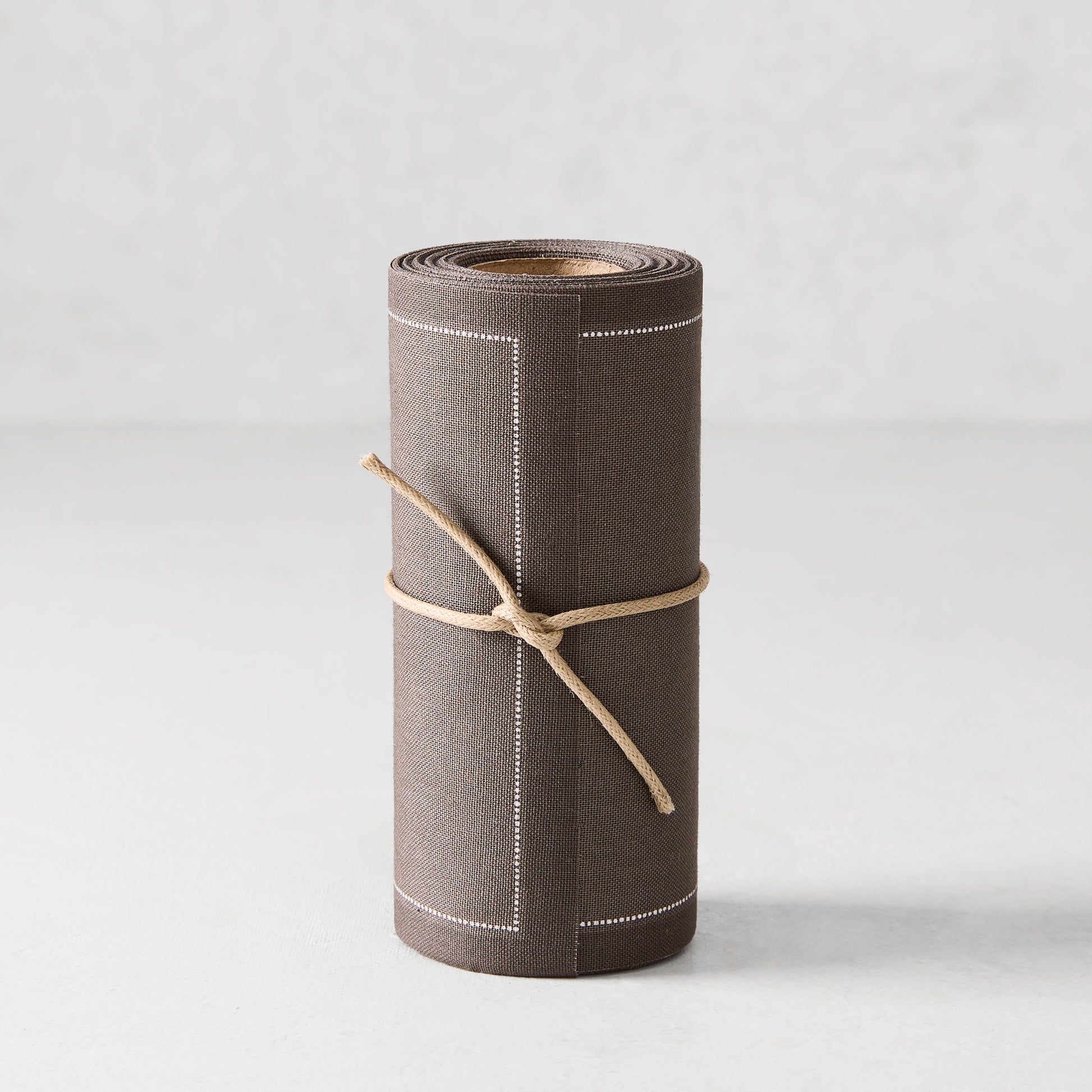Roll of 50 anthracite grey tear-off cotton cocktail napkins with white stitched border, tied with twine.