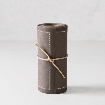 Roll of 50 anthracite grey tear-off cotton cocktail napkins with white stitched border, tied with twine.