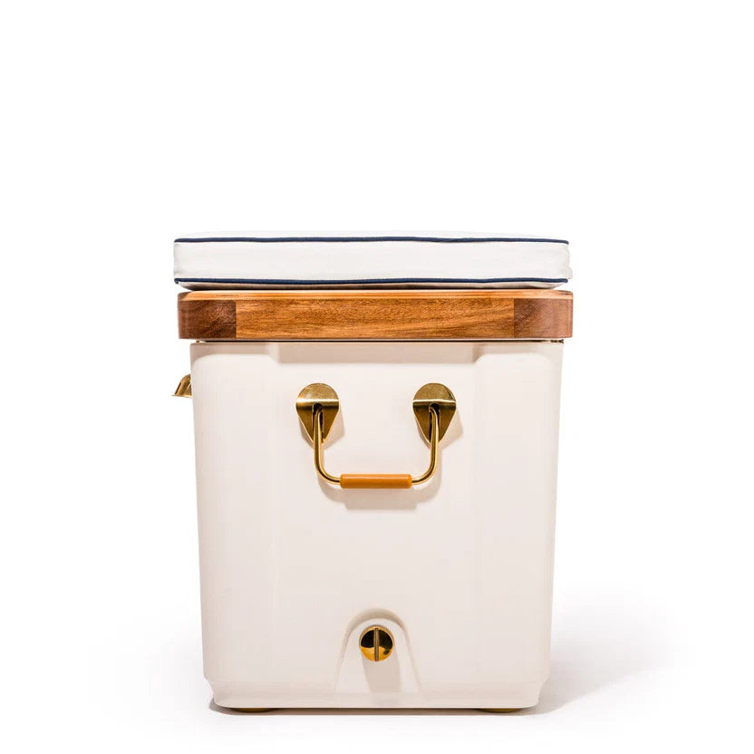 Antique white Hemingway cooler with acacia wood lid, brass handles, and a white cushion with navy trim.