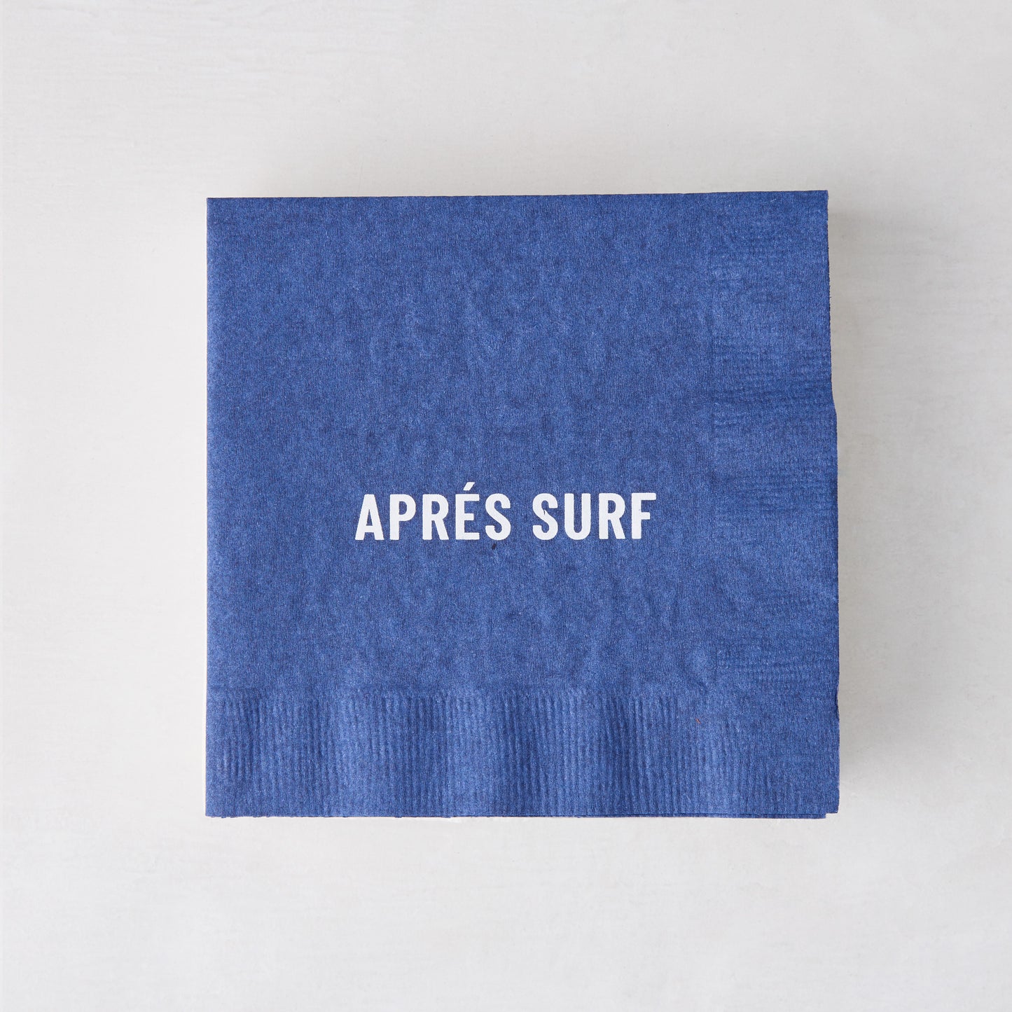 Blue 5.5" square paper cocktail napkin with "APRÉS SURF" in white text.