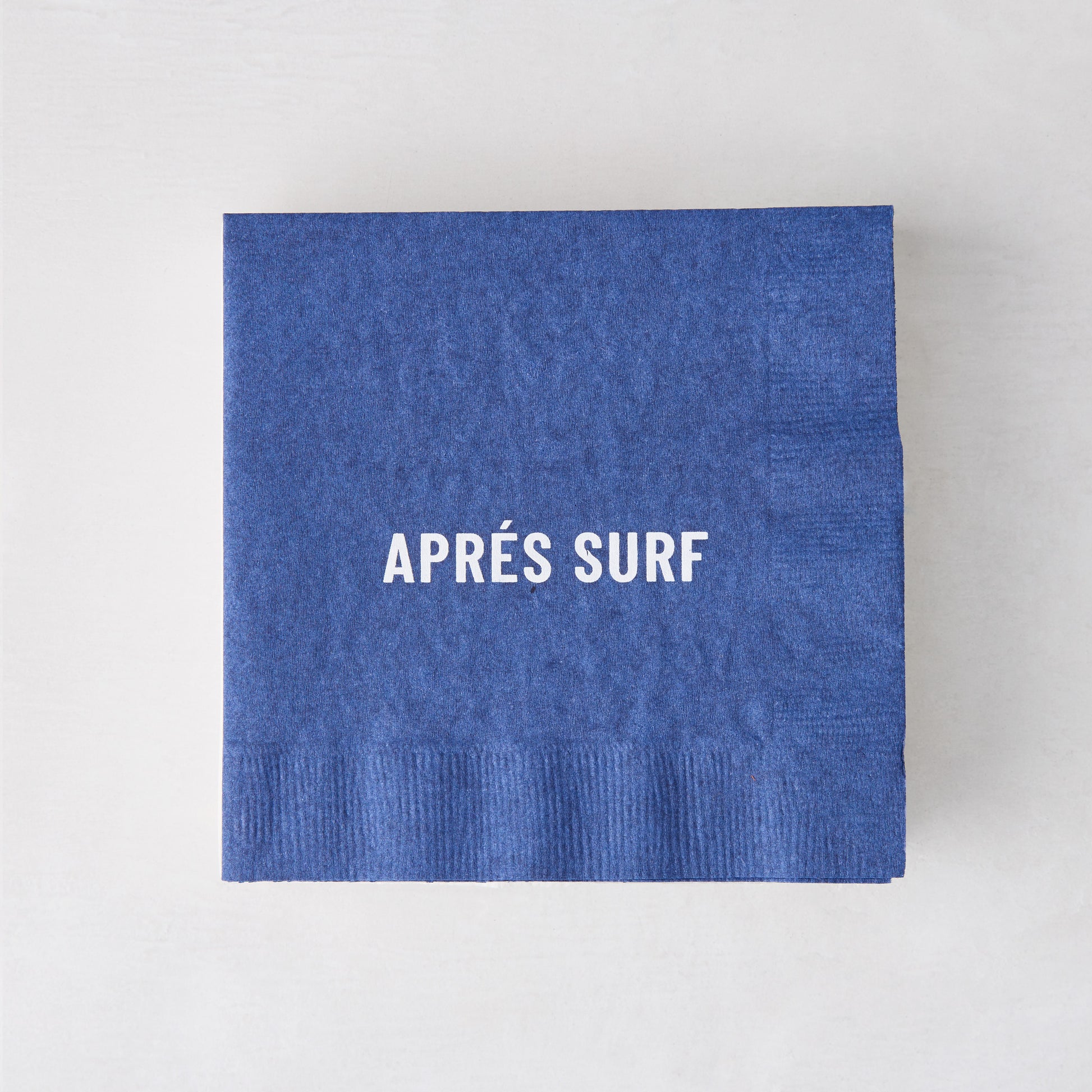 Blue 5.5" square paper cocktail napkin with "APRÉS SURF" in white text.