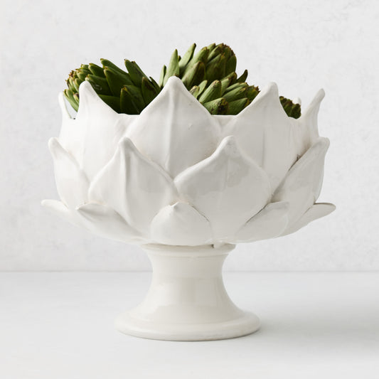 White ceramic footed bowl shaped like an artichoke, 14 inches wide, filled with fresh green artichokes.