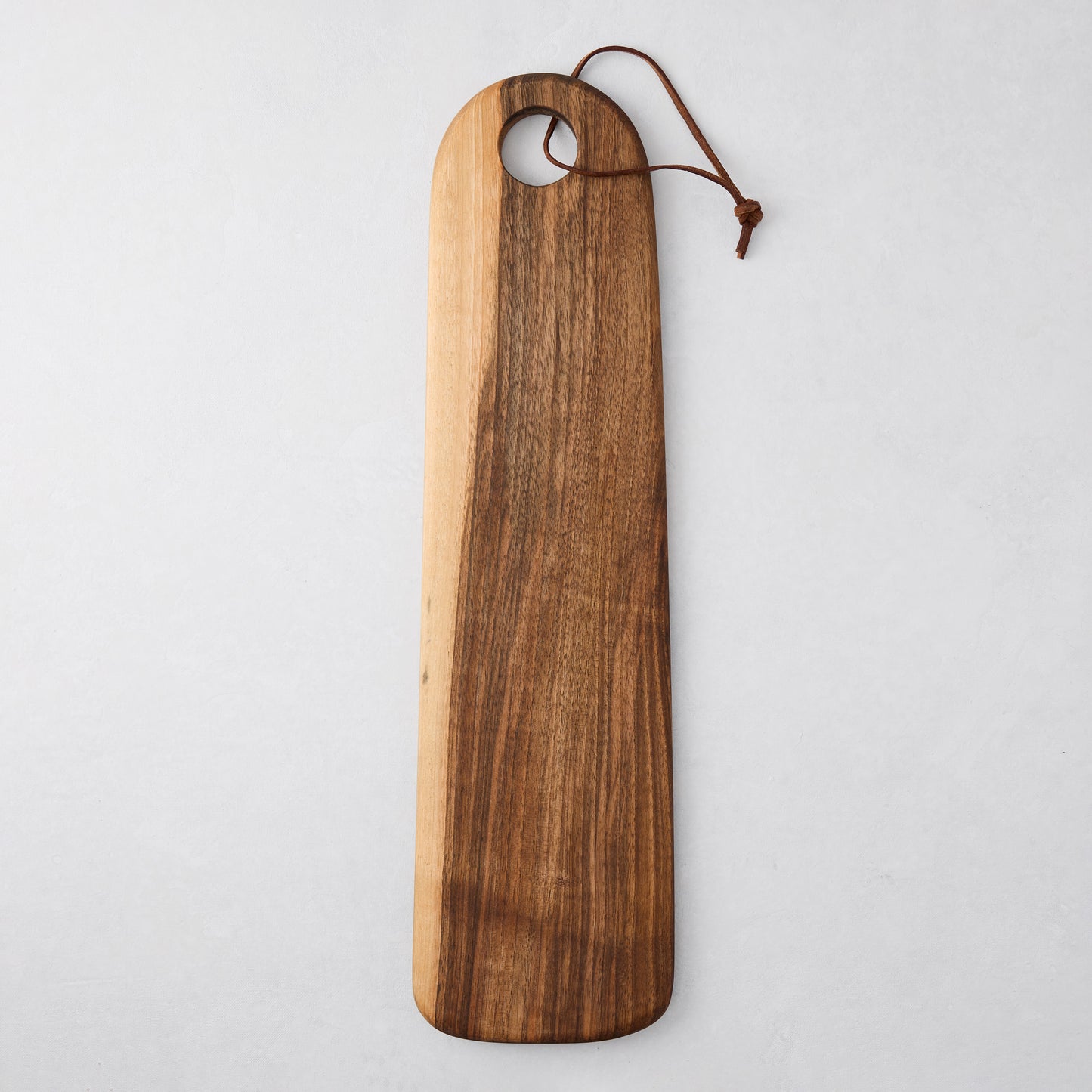 Long oval olive wood serving board with natural grain, hole, and leather cord.