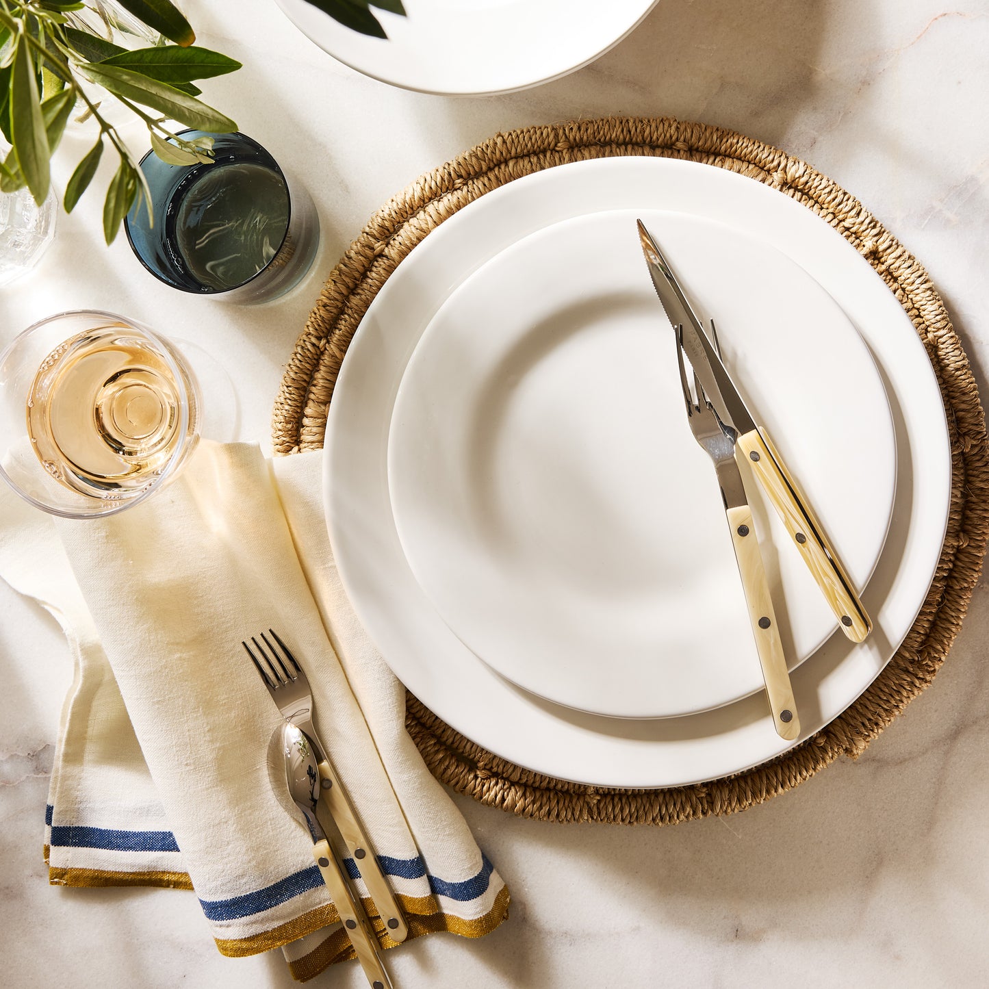 Artisan creamy white stoneware salad plate on a woven placemat with cutlery, napkin, and drinks.