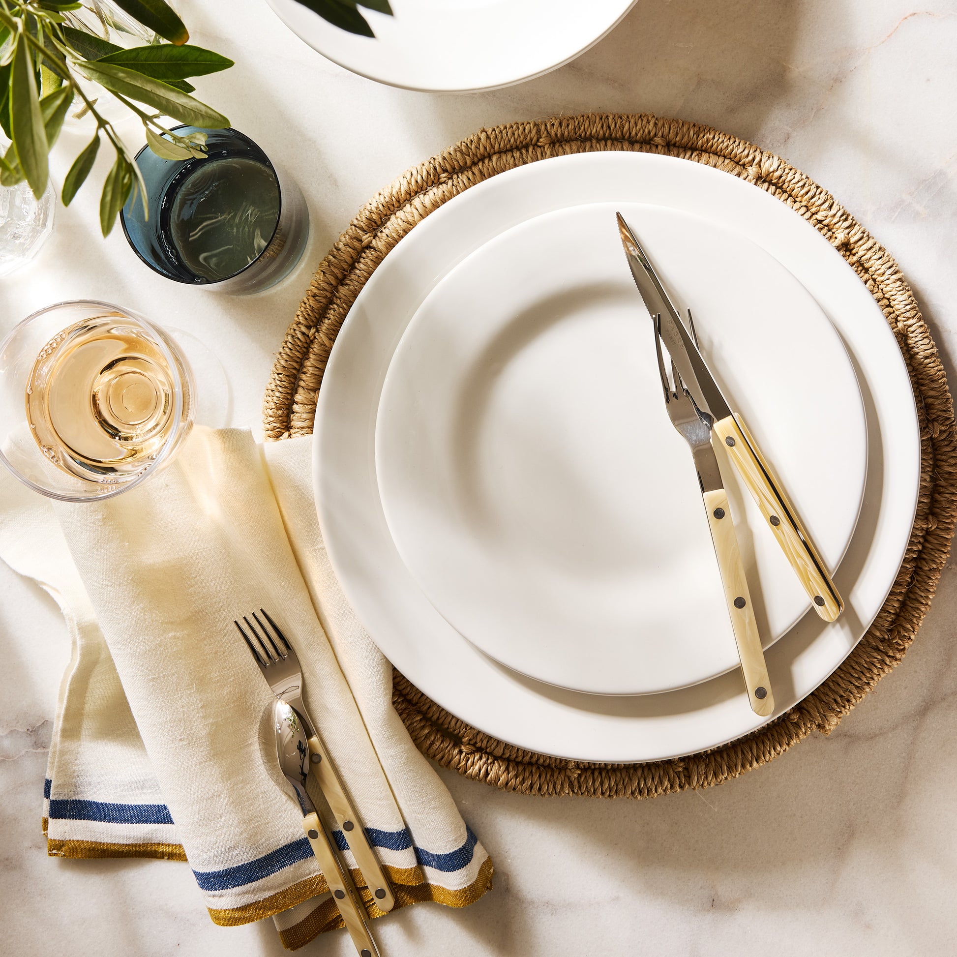 Artisan creamy white stoneware salad plate on a woven placemat with cutlery, napkin, and drinks.