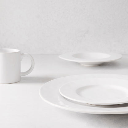 Creamy white Artisan stoneware salad plate with wide lip, stacked on a dinner plate, with a mug and bowl.