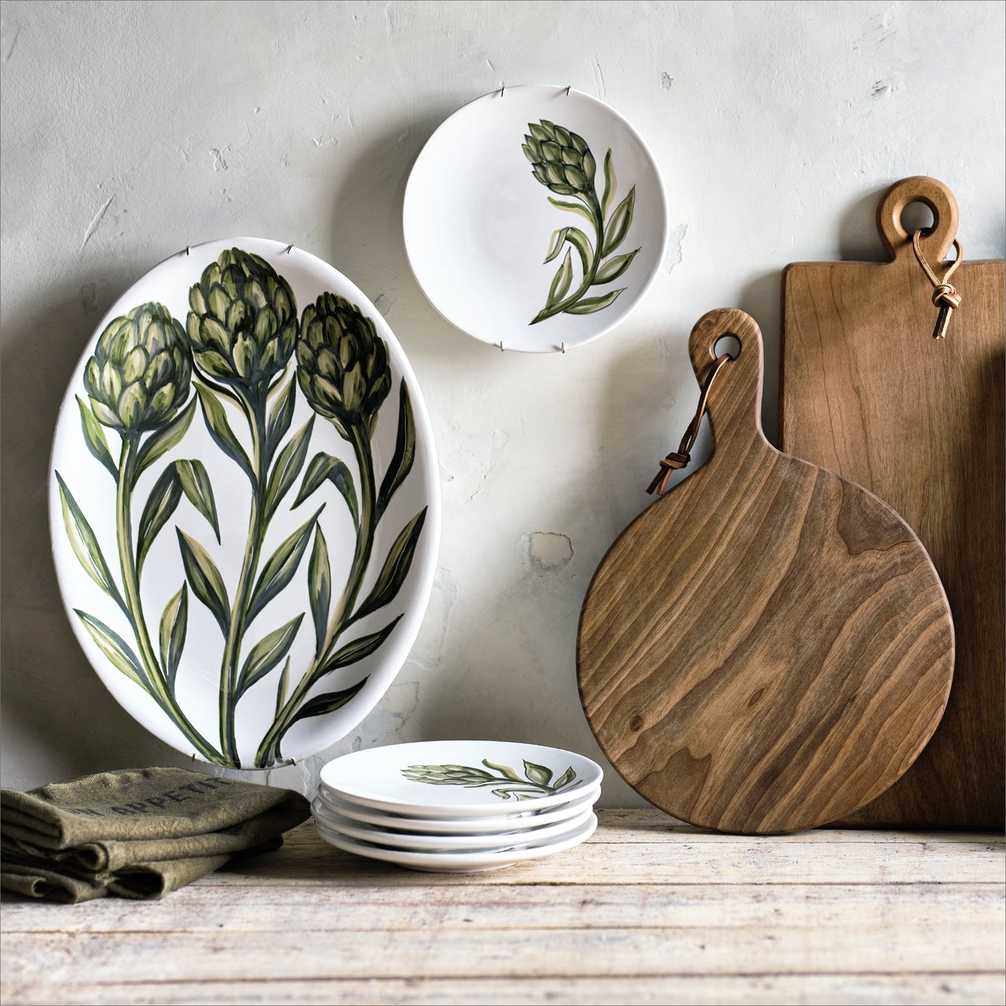 Rectangular walnut wood serving board with leather hanging cord, displayed next to round wooden boards and artichoke plates.