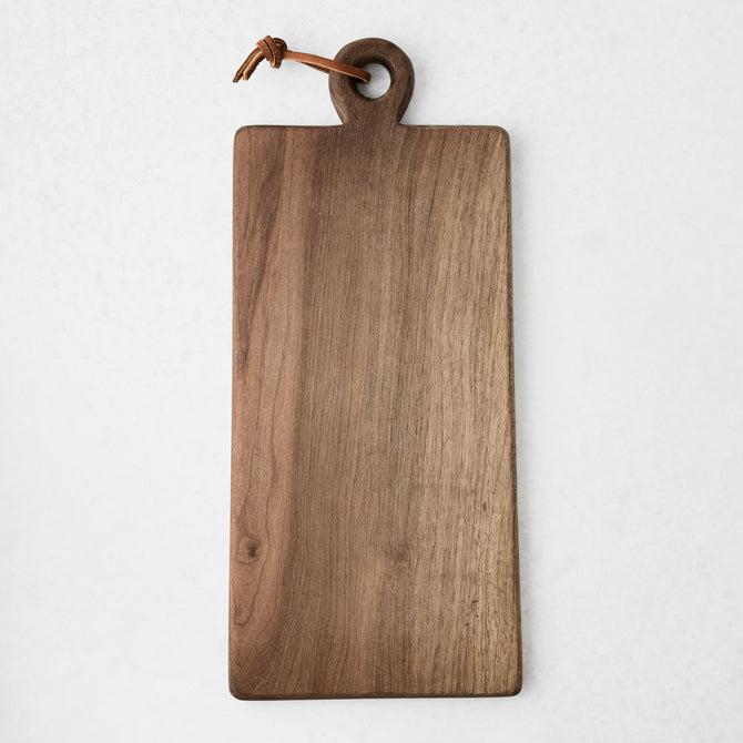 Artisan rectangular walnut wood serve board with a round handle and brown leather cord.