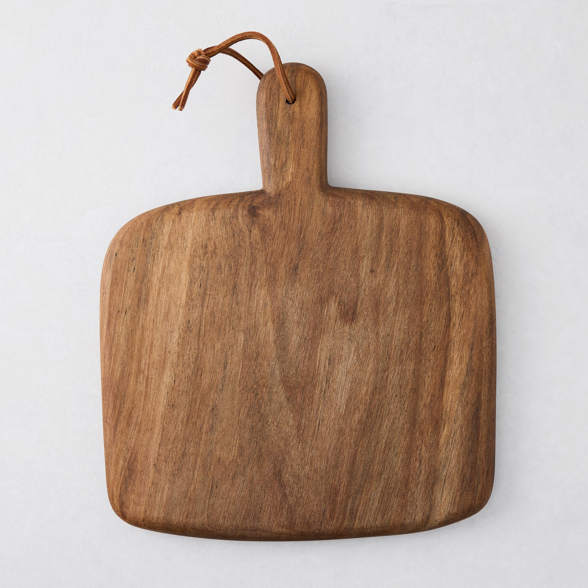Artisan walnut wood serving board with a handle and leather hanging cord.