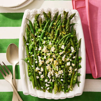 White ceramic serving dish filled with asparagus, green beans, peas, feta, and lemon zest.
