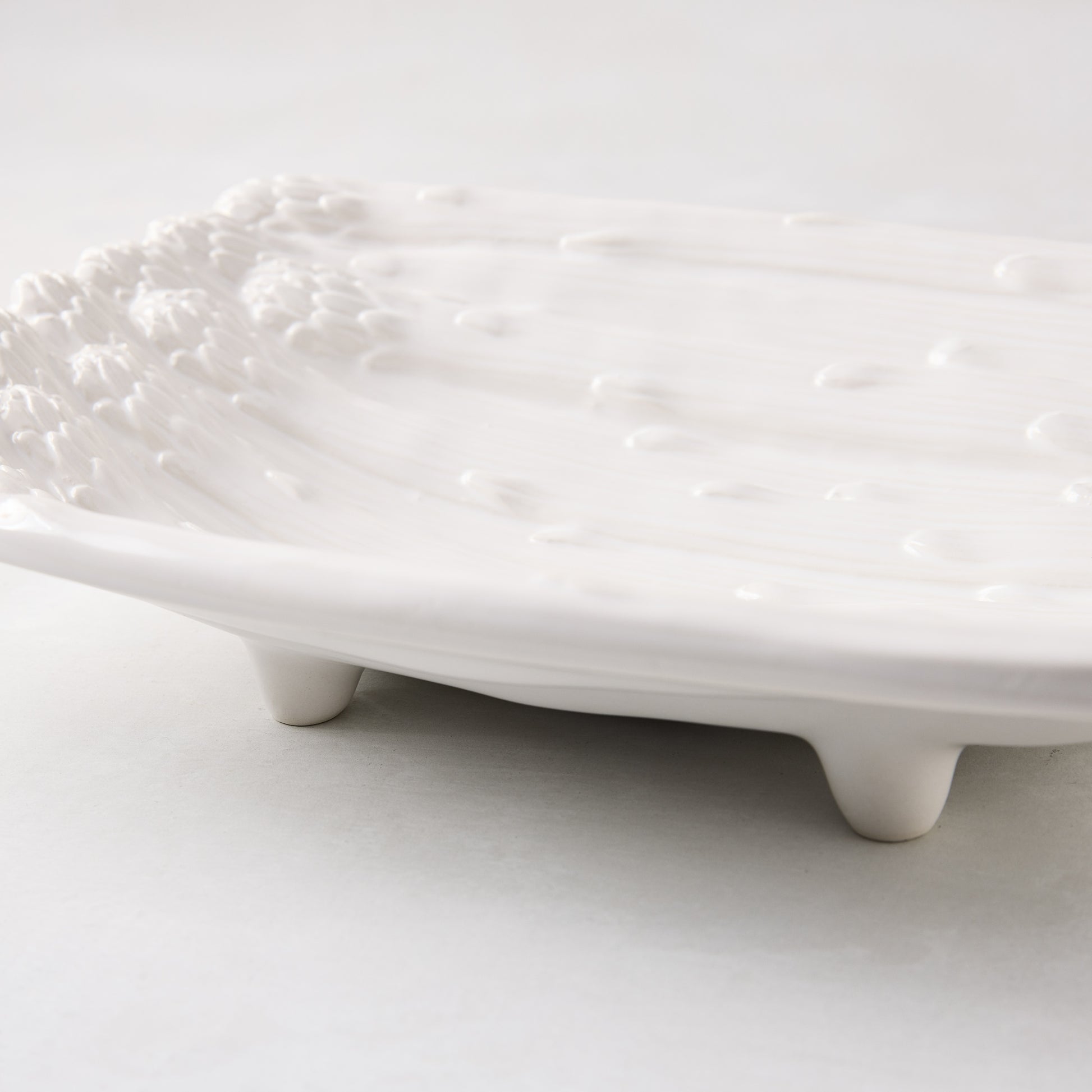 White ceramic serving dish with raised asparagus design and small feet.