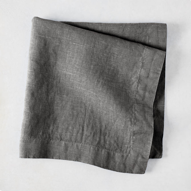 Asphalt HG Signature hand-dyed linen napkin, 22-inch square, folded, dark gray with visible texture.