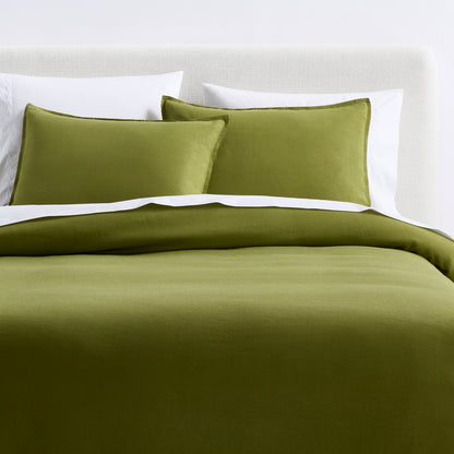Avocado green washed linen duvet cover and two matching shams on a bed with white accent pillows.