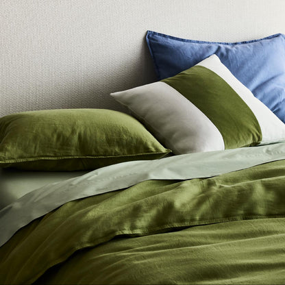 Avocado green washed linen duvet cover and sham set with layered blue and striped accent pillows on a bed.