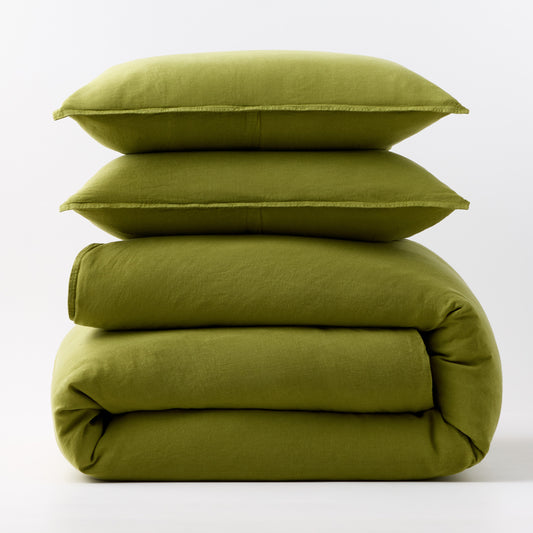 Stacked avocado green European washed linen duvet cover and two matching pillow shams on a white background.