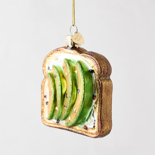 Hand-painted glass and resin avocado toast Christmas ornament with glittery brown crust and green avocado slices.