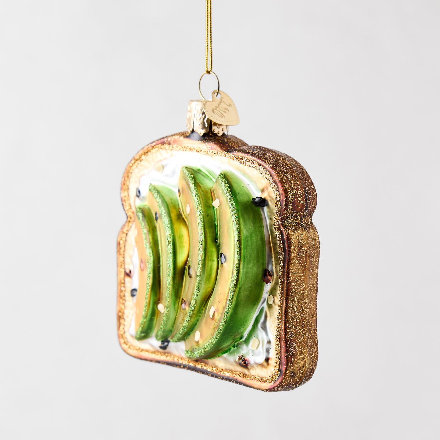Hand-painted glass and resin avocado toast Christmas ornament with glittery brown crust and green avocado slices.