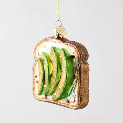 Hand-painted glass and resin avocado toast Christmas ornament with glittery brown crust and green avocado slices.