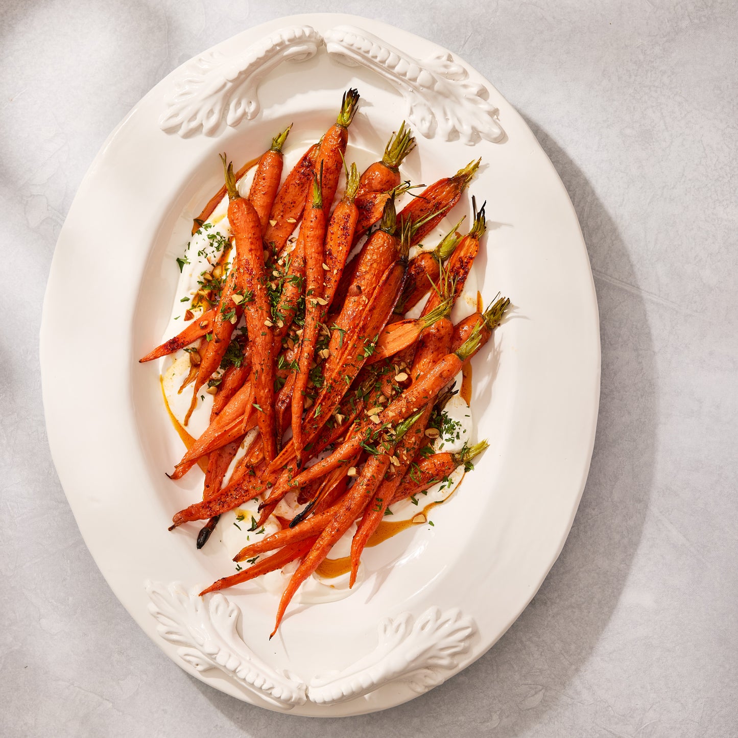 White Baccello Ceramic Oval Serving Platter with artisanal handles, filled with roasted carrots and sauce.