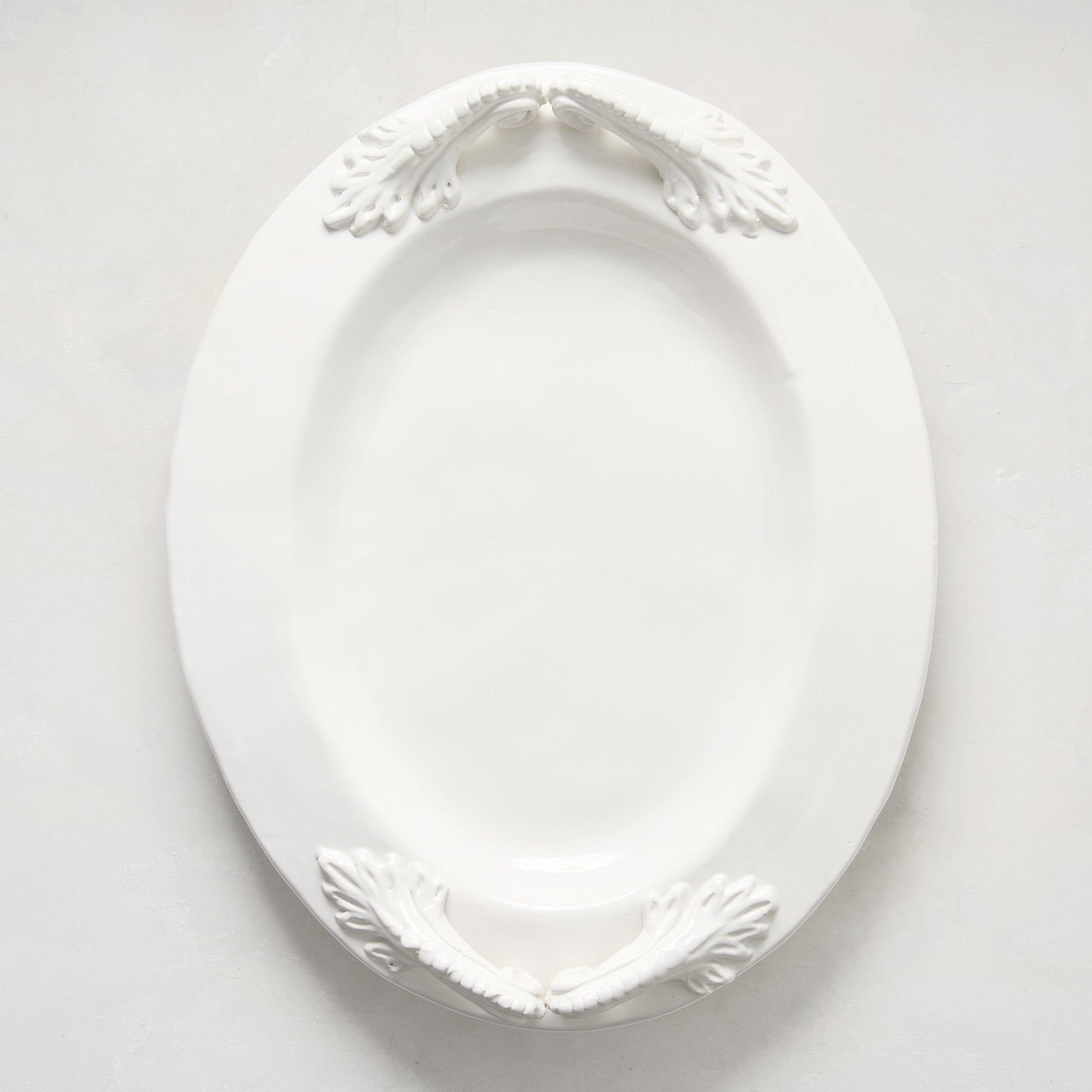 White ceramic oval serving platter with decorative artisanal handles.