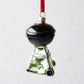 Hand-painted glass and resin Backyard Grill Christmas ornament, black and green with glitter, hanging from a red ribbon.