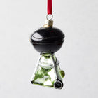 Hand-painted glass and resin Backyard Grill Christmas ornament, black and green with glitter, hanging from a red ribbon.