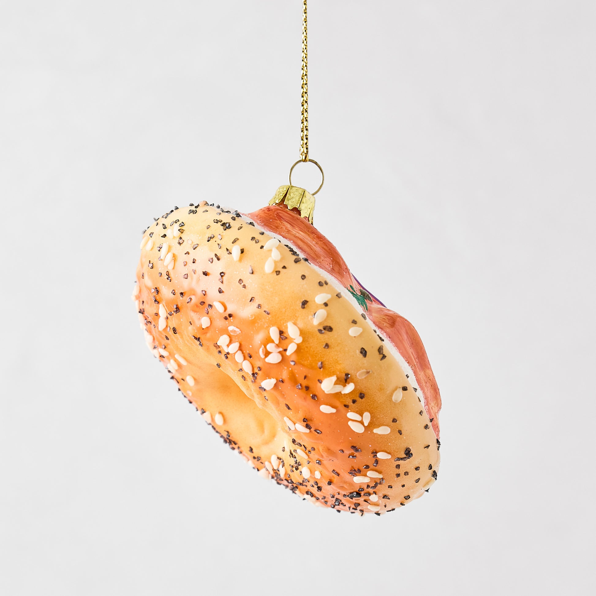 Hand-painted glass and resin bagel and lox Christmas ornament with sesame seeds and glitter accents.