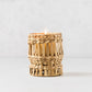 Bali Extra Small Woven Hyacinth Hurricane with a lit candle inside, natural light brown basket weave.