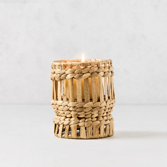 Bali Extra Small Woven Hyacinth Hurricane with a lit candle inside, natural light brown basket weave.