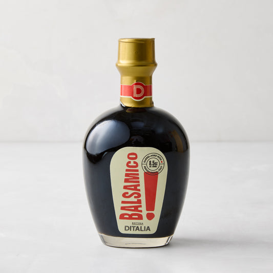 Dark balsamic vinegar in a clear glass bottle with a gold cap and red and cream label.