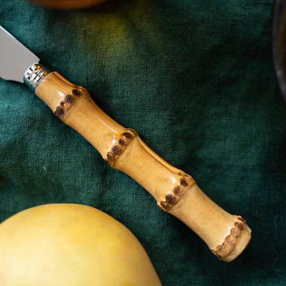 Bamboo 5-piece flatware set with natural bamboo handle and 18/10 stainless steel knife on a dark green cloth.