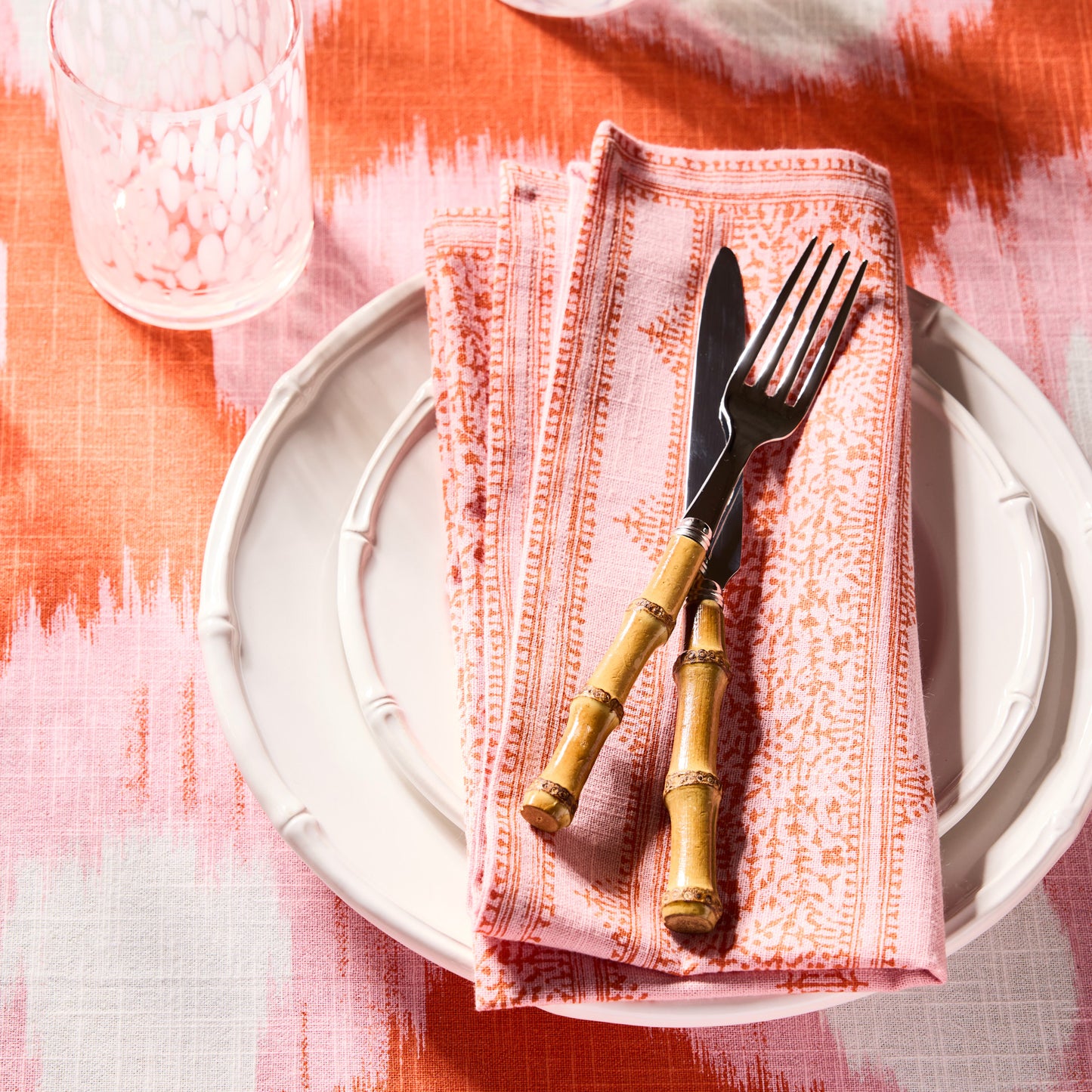 Bamboo 5-piece flatware set with 18/10 stainless steel knife and fork on a pink patterned napkin and white plate.