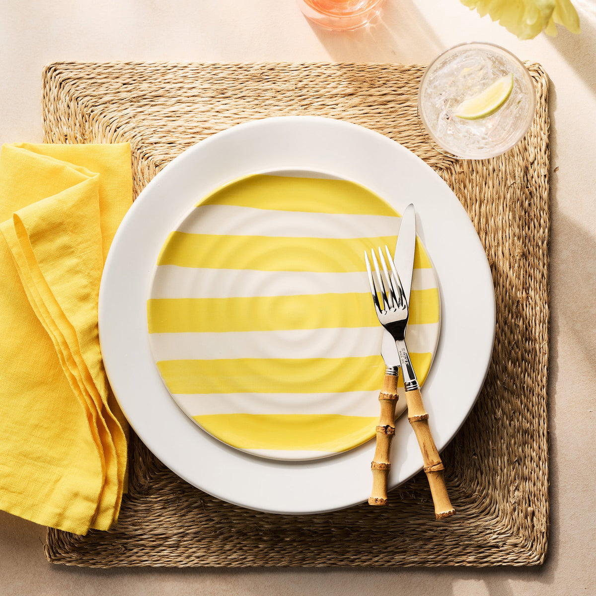 Stainless steel fork and knife with natural bamboo handles placed on a yellow striped plate and woven placemat.