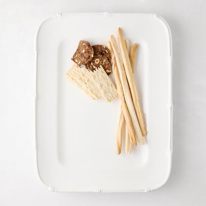 White ceramic rectangular serving platter with bamboo-molded edge, holding crackers and breadsticks.