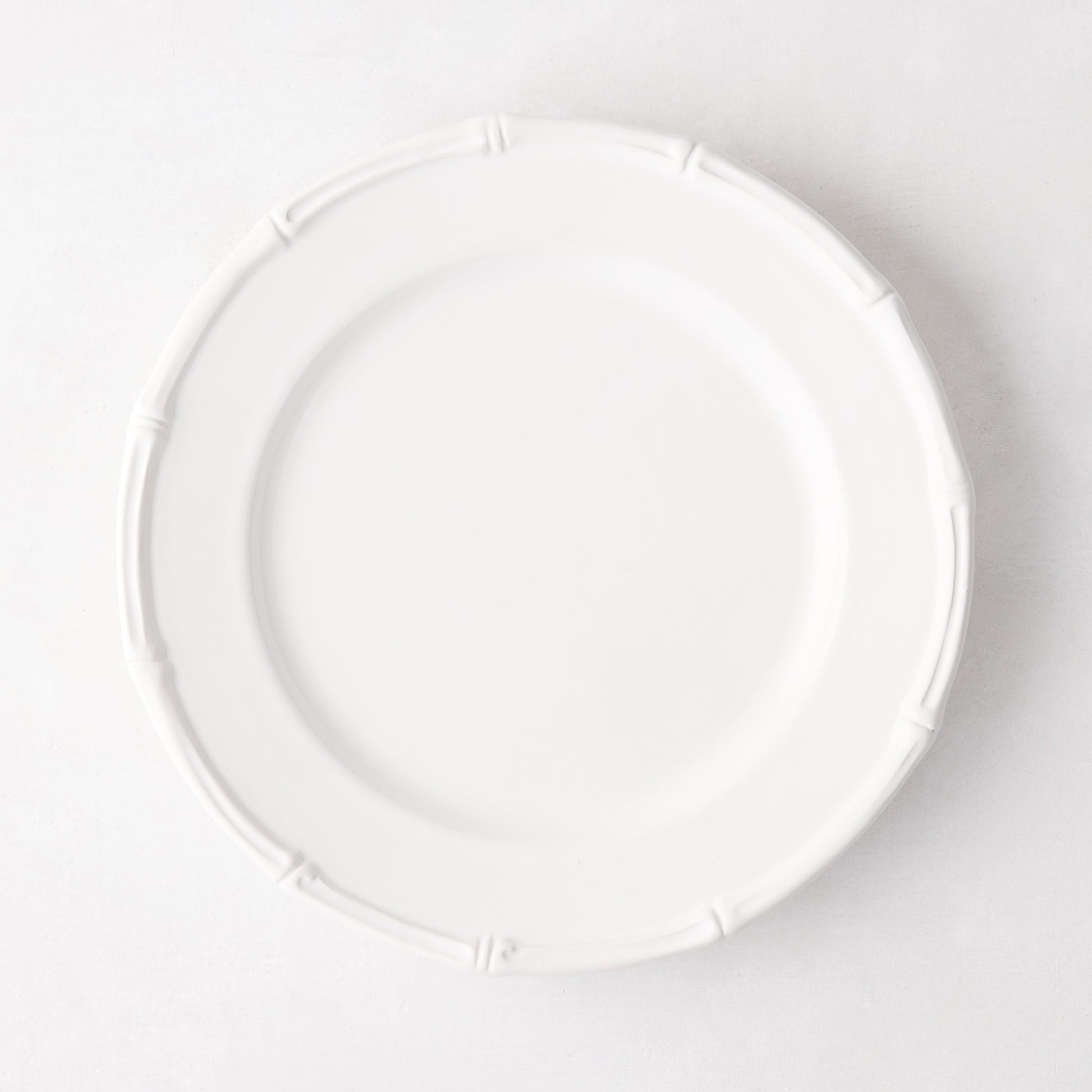 White ceramic salad plate with molded bamboo detailing on the rim.