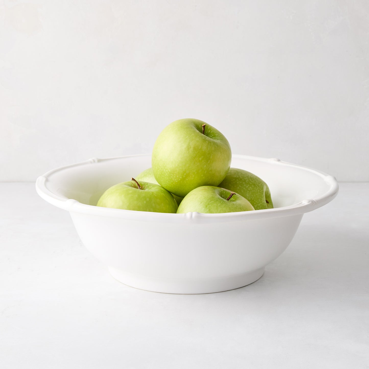 White ceramic serve bowl with molded bamboo detailing, filled with green apples.