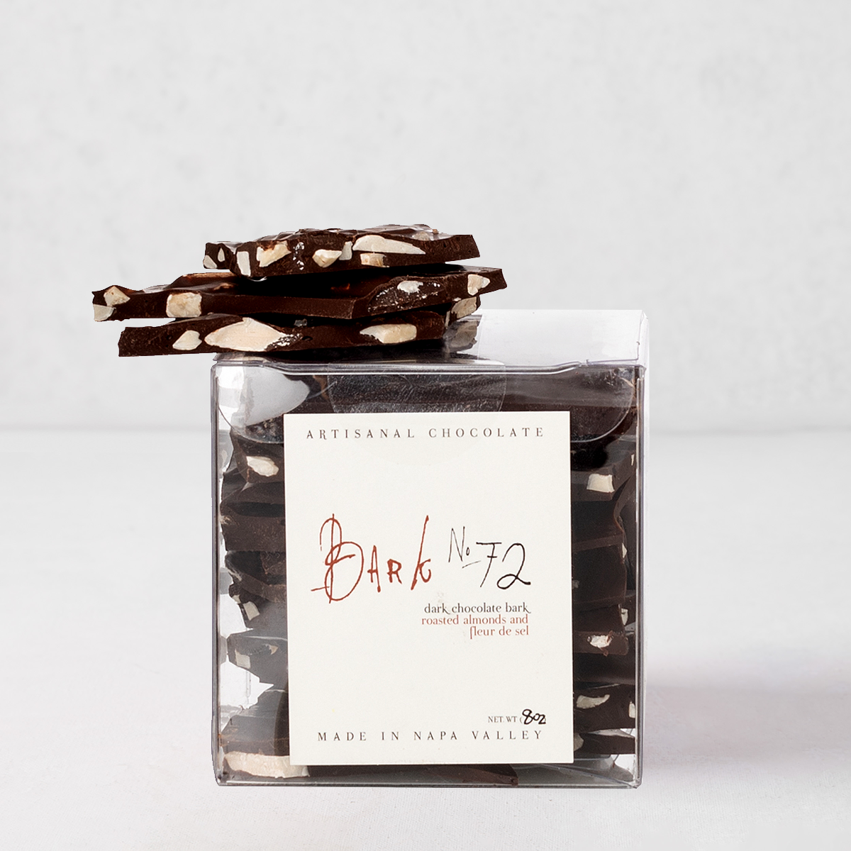 Bark 72 Dark Chocolate Almond Bark, 8oz, in a clear container with pieces stacked on top.