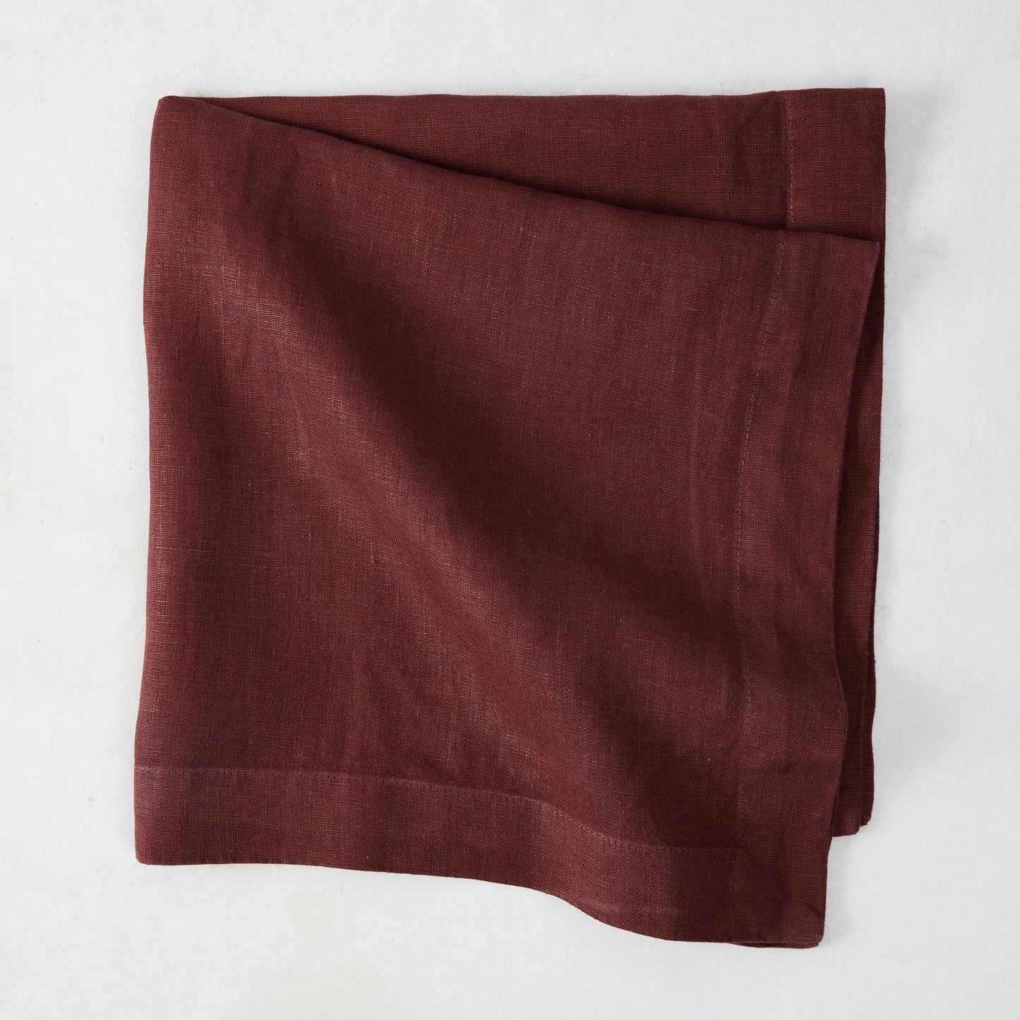 Barnwood HG Signature hand-dyed 22-inch maroon linen napkin, folded on a white surface.