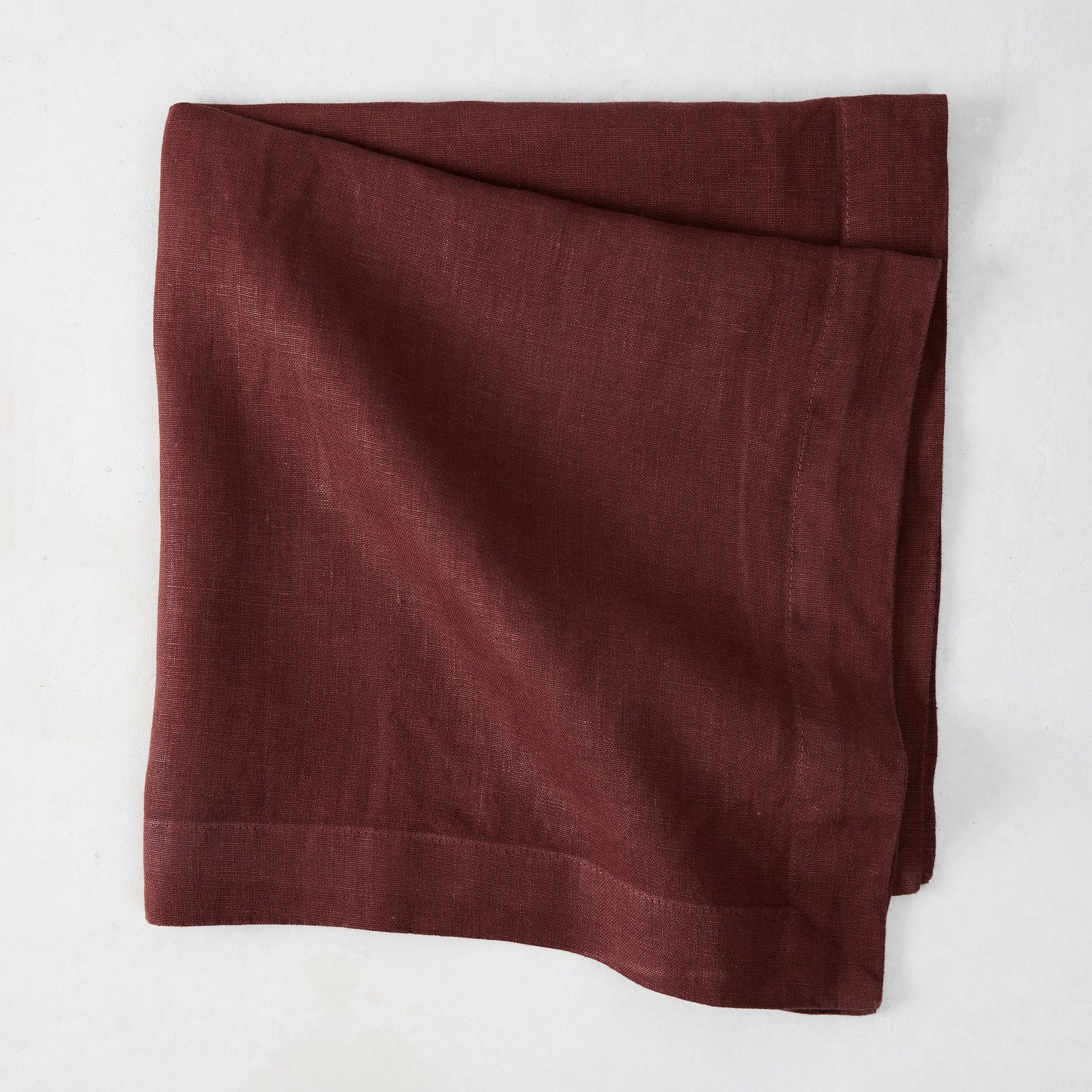 Barnwood HG Signature hand-dyed 22-inch maroon linen napkin, folded on a white surface.