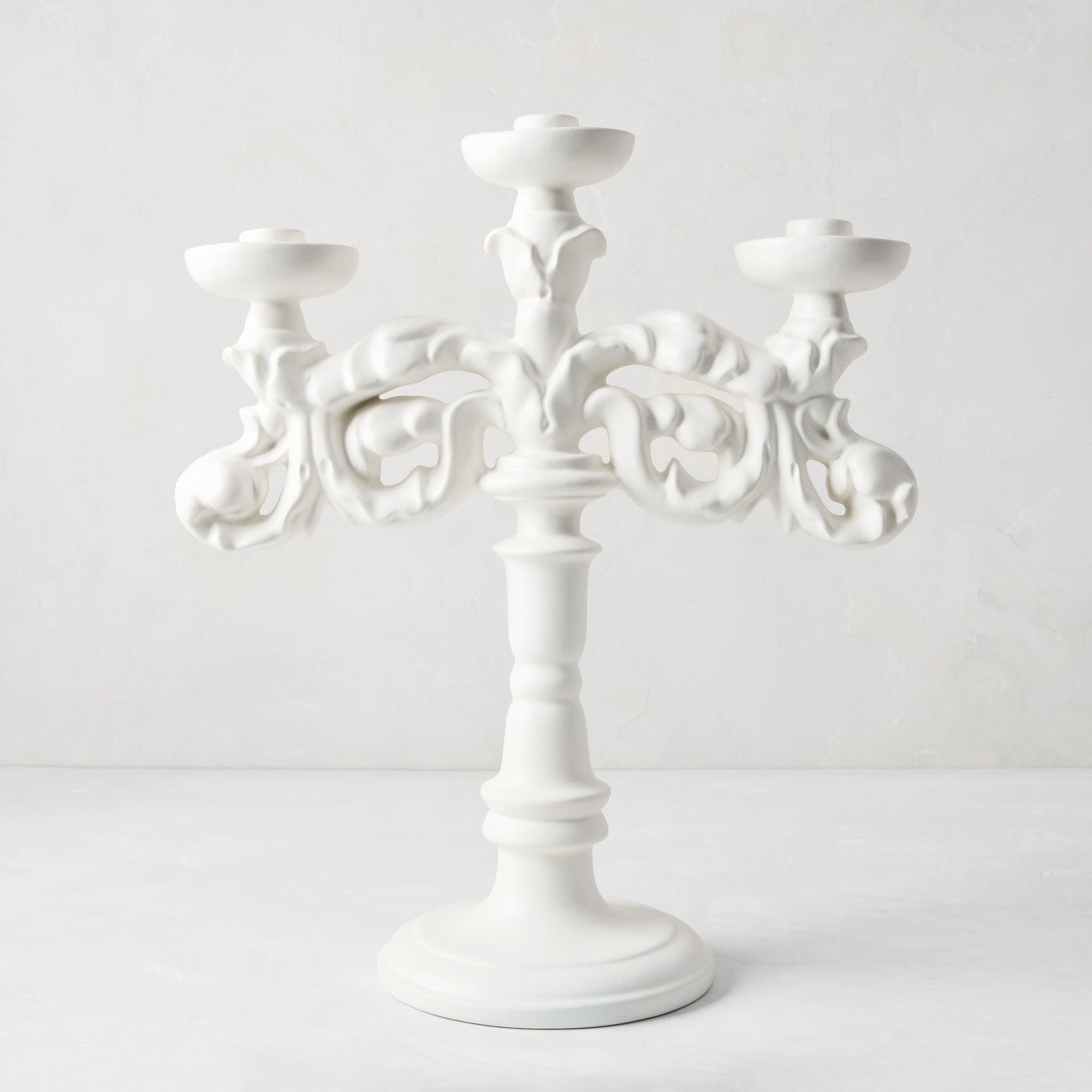 Baroque matte white ceramic candelabra, 18"H, with three candle holders and ornate scrollwork.