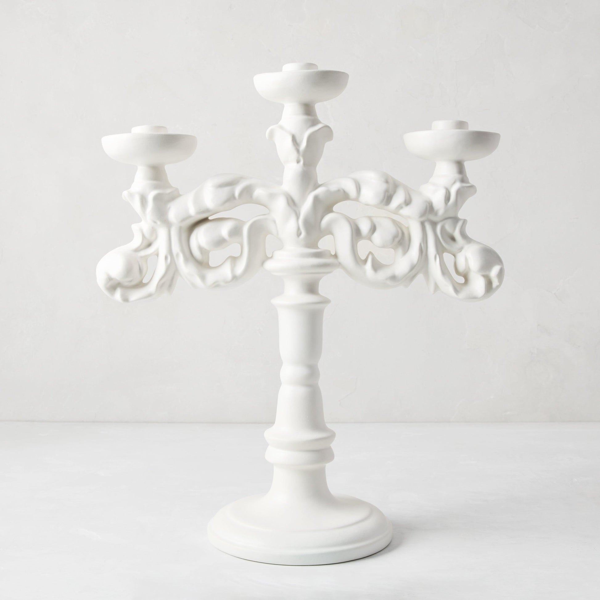 Baroque matte white ceramic candelabra, 18"H, with three candle holders and ornate scrollwork.